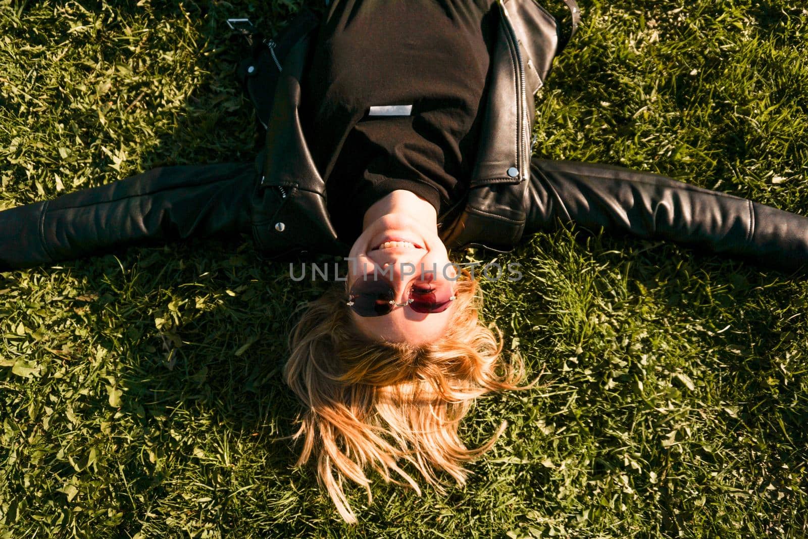 Beautiful healthy Young Woman lying and relaxing on the green grass. Happy smiling blonde in sunglasses on a summer day.