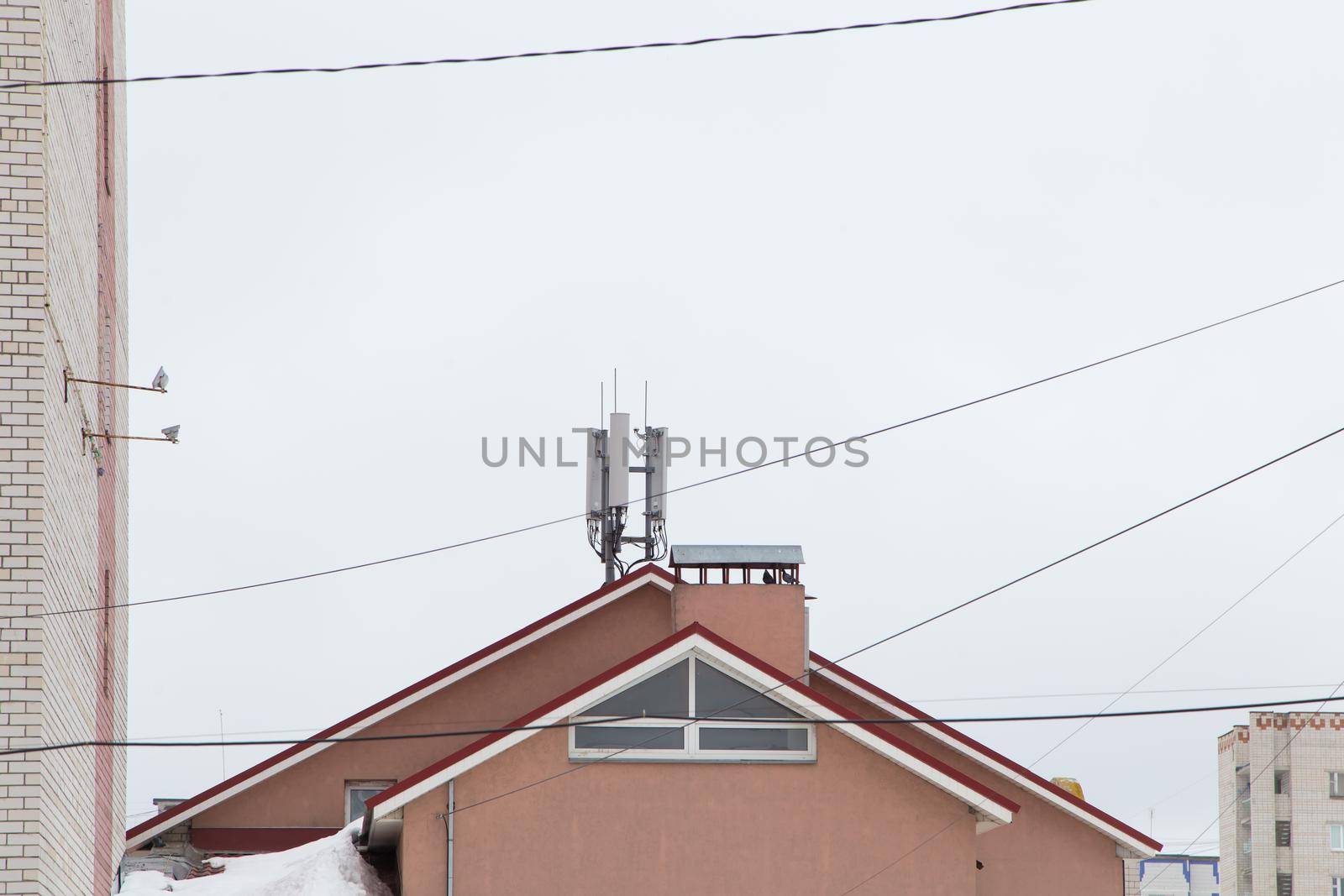 Telecommunication antenna next to a residential building. Cellular and telephone communications. Chimney against the gray sky. Electric wires are located in different places.