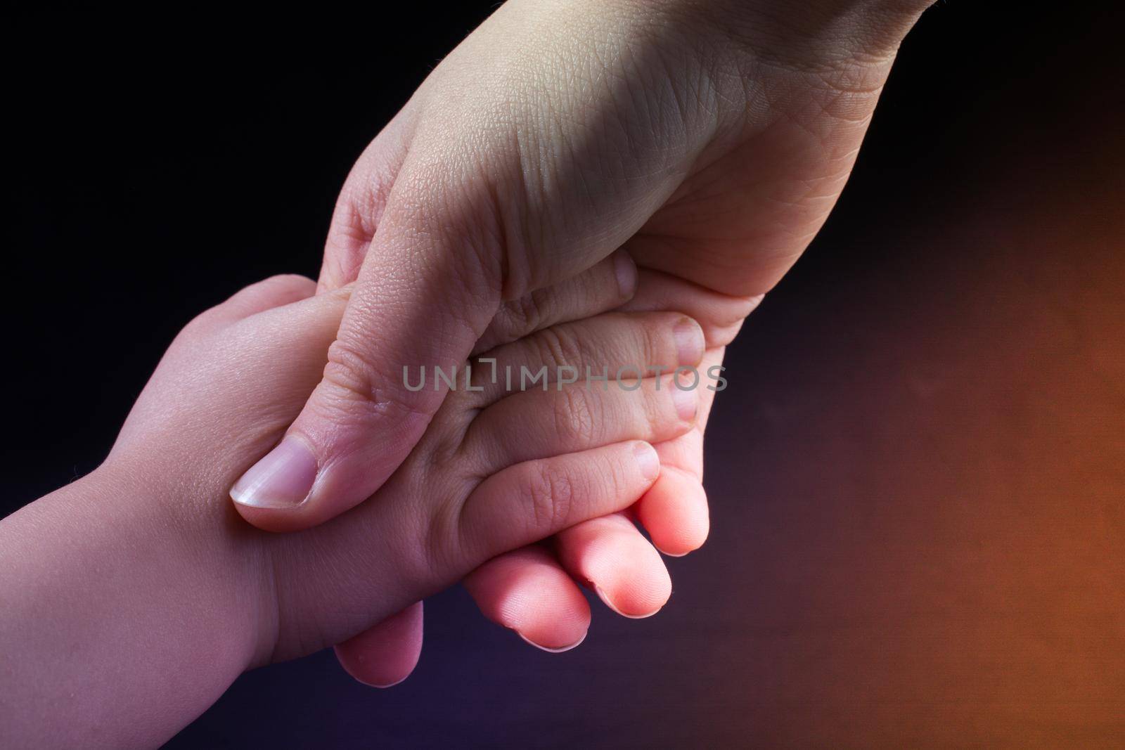 Adult and child hold hands in black background