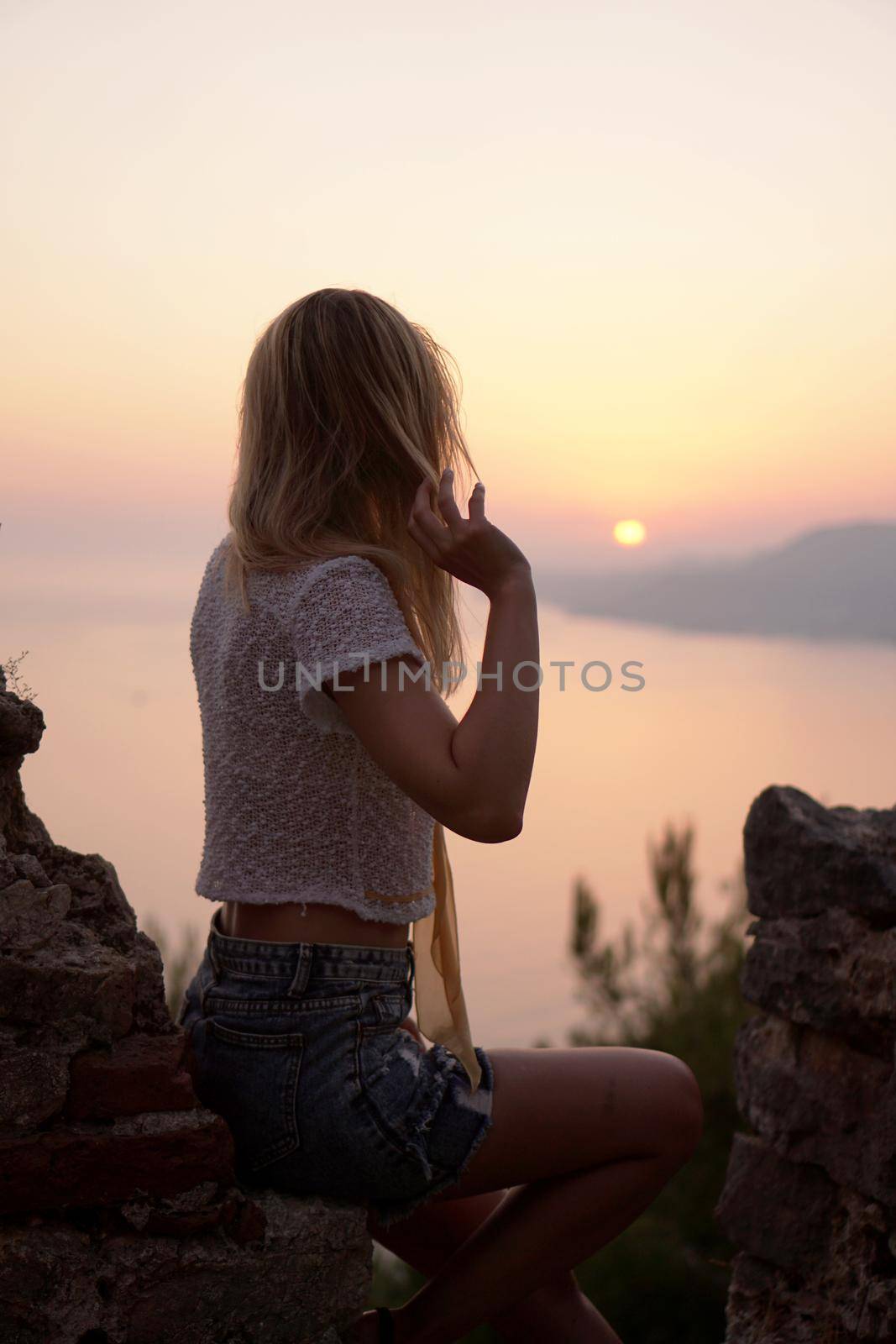 The girl looks at the sea sunset from a high point. Vertical photo by natali_brill