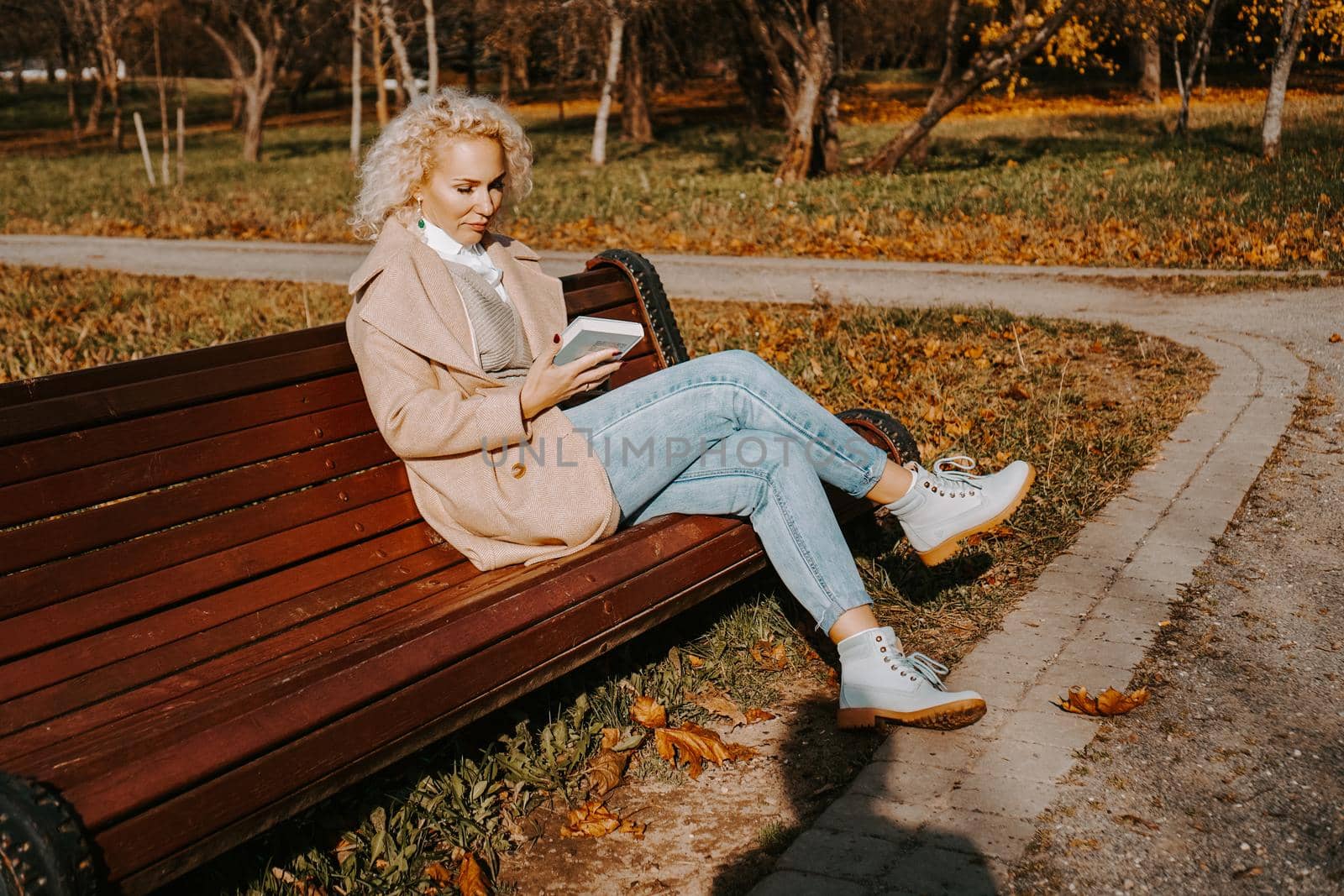 Woman reading a book on a park bench, leisure time in autumn park
