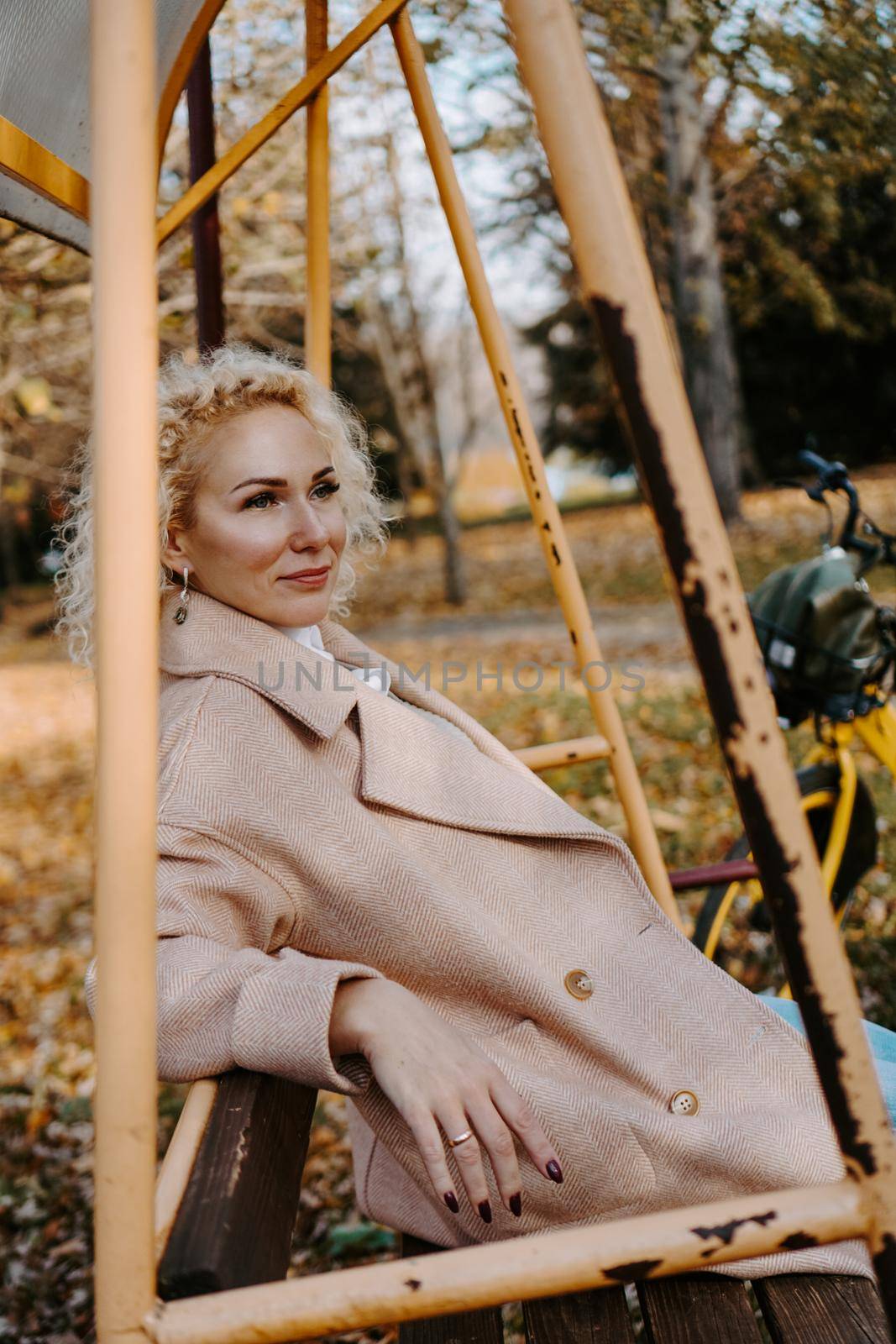 Portrait of smilling middle aged woman sitting and swinging on swing in autumn park