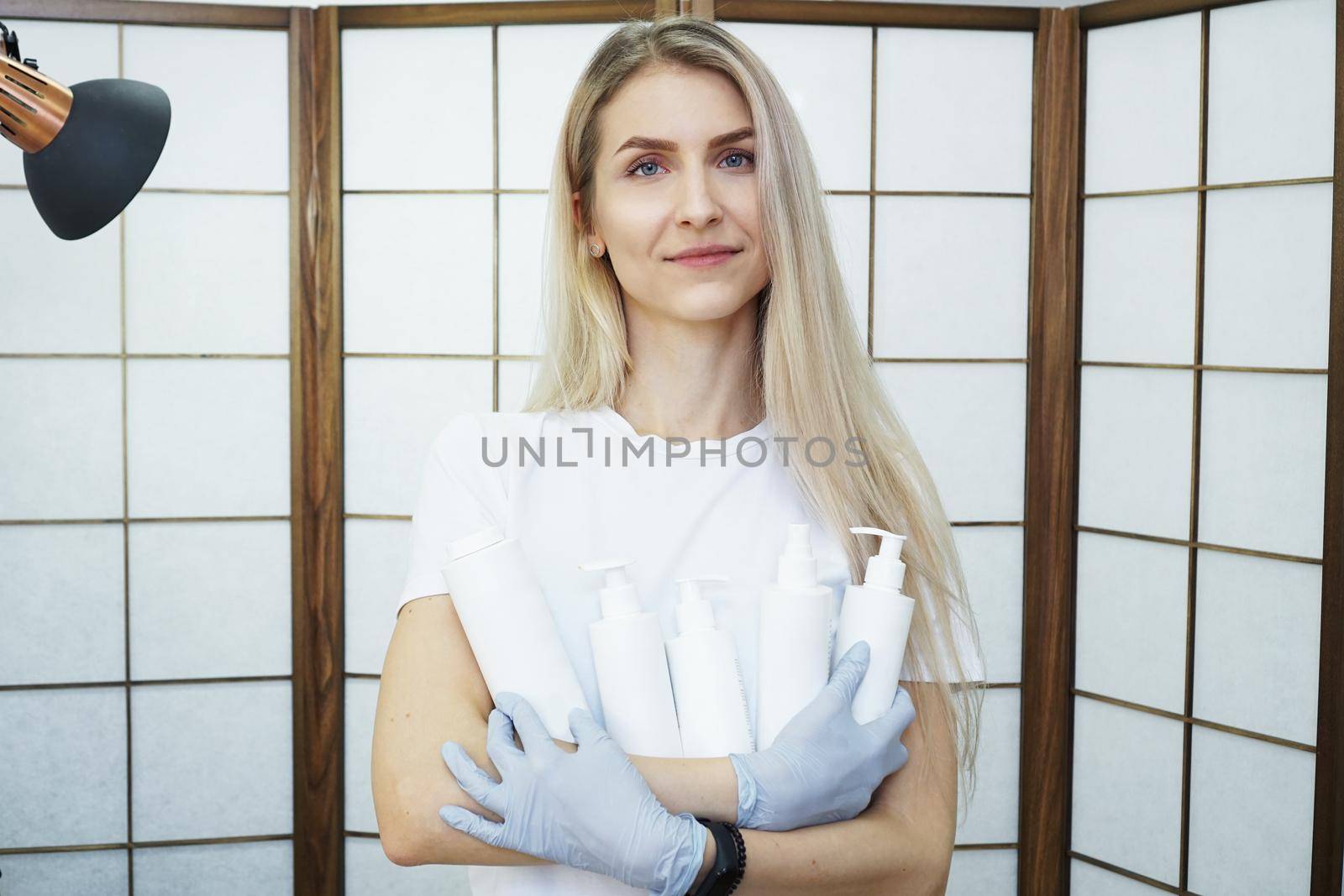 Master holds set of cosmetics - white bottles - Beautiful woman master in a beauty salon