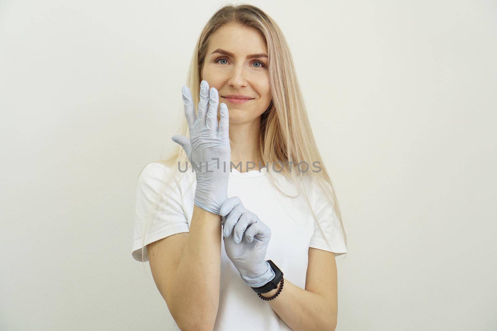 Young energetic beautiful girl puts on gloves. Joyful friendly woman is waiting for the client and getting ready for work. Beauty salon specialist.