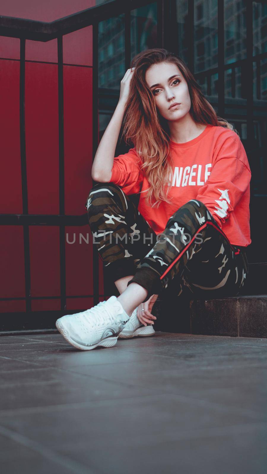 Fashion model wearing red hoodie with the inscription los angeles posing in the city at parking. Fashion urban outfit. Casual everyday clothing style