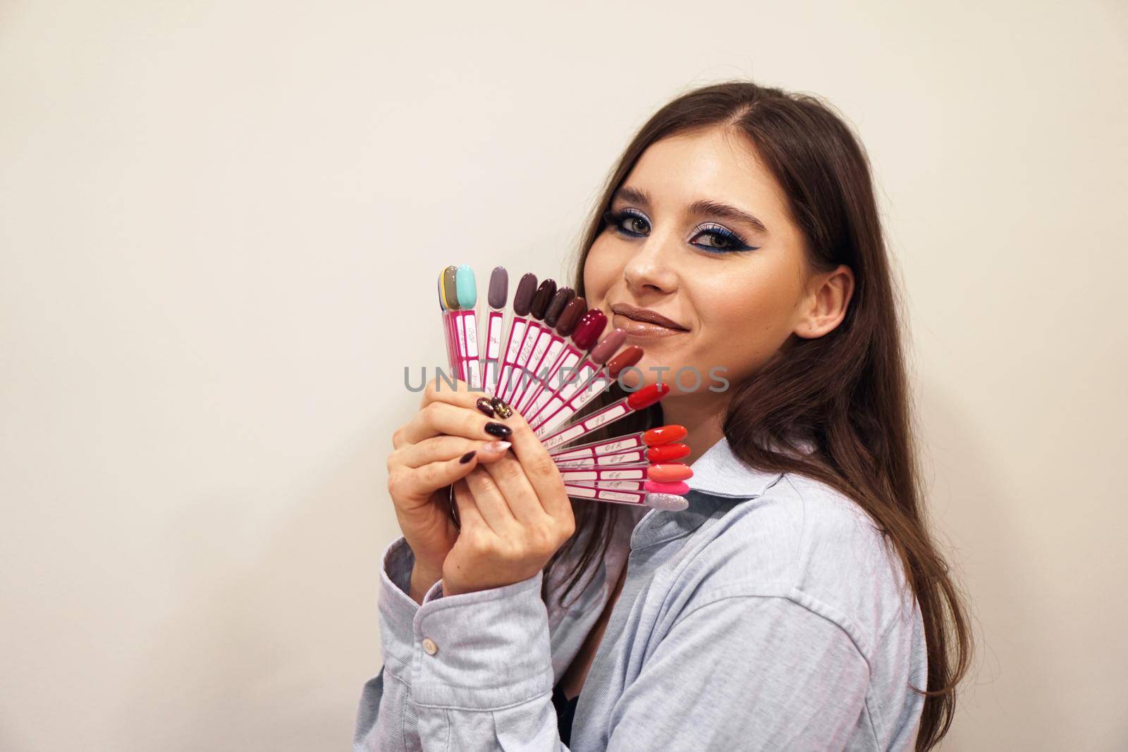 Pretty young woman smiling, holding a manicure and pedicure nail polish palette in a hand. Cosmetic products. Beauty salon.