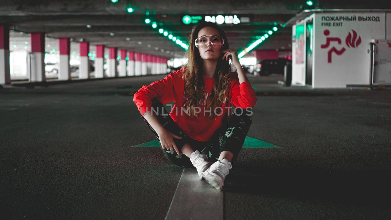 Pretty young woman sitting on car parking. Wearing stylish urban outfit by natali_brill