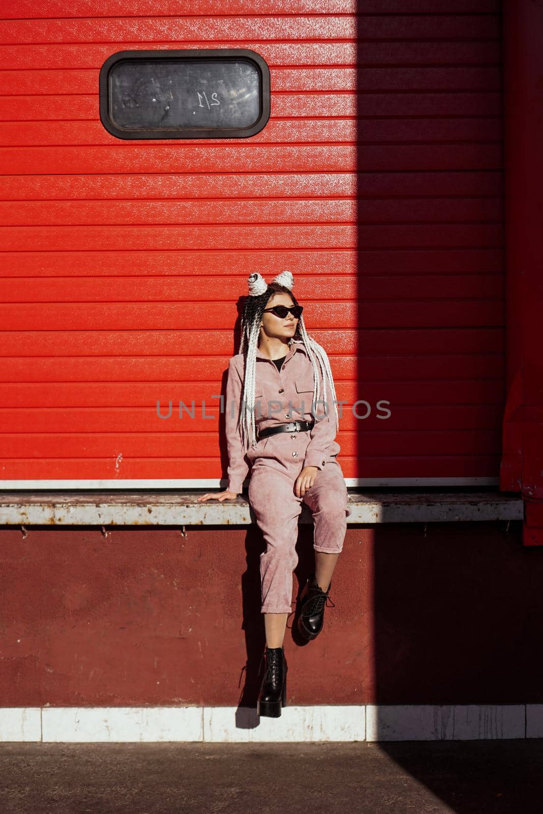 Beautiful girl over urban wall. Sunny day. Girl in sunglasses and pink jumpsuit