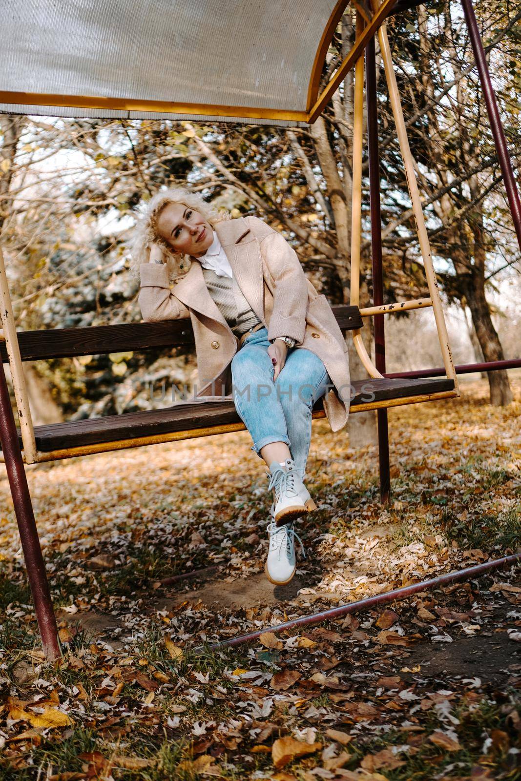 Portrait of smilling middle aged woman sitting and swinging on swing in park by natali_brill