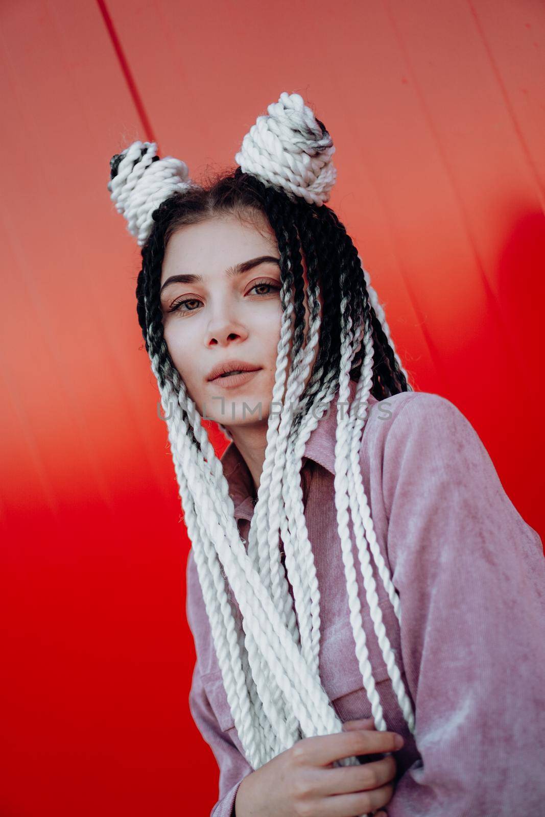 Portrait of beautiful cool girl with Senegalese pigtails and dreadlocks over red wall