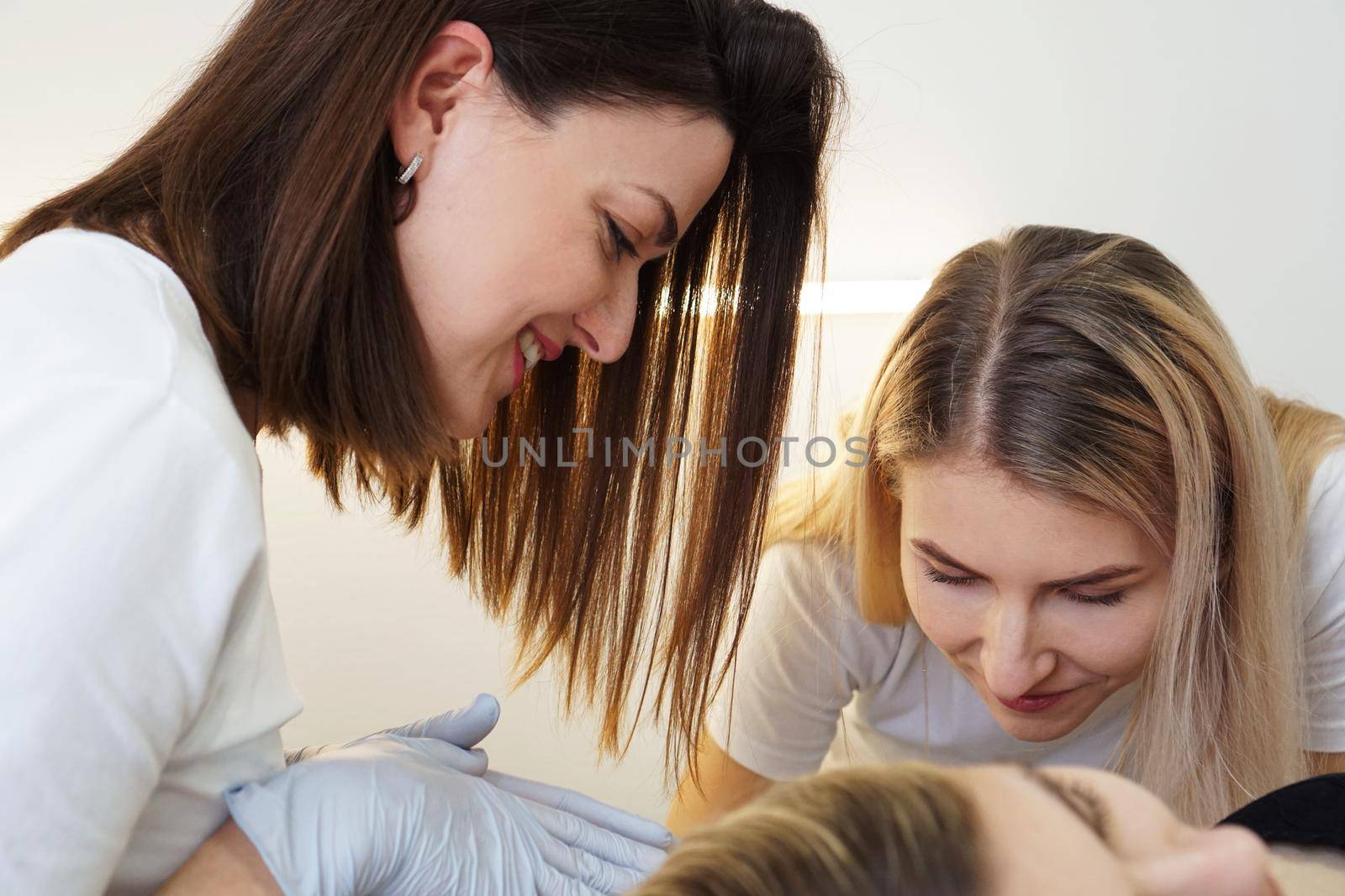 Two cheerful confident cosmetologists doing hair removal. Two happy women do the armpit depilation procedure. The concept of teaching depilation