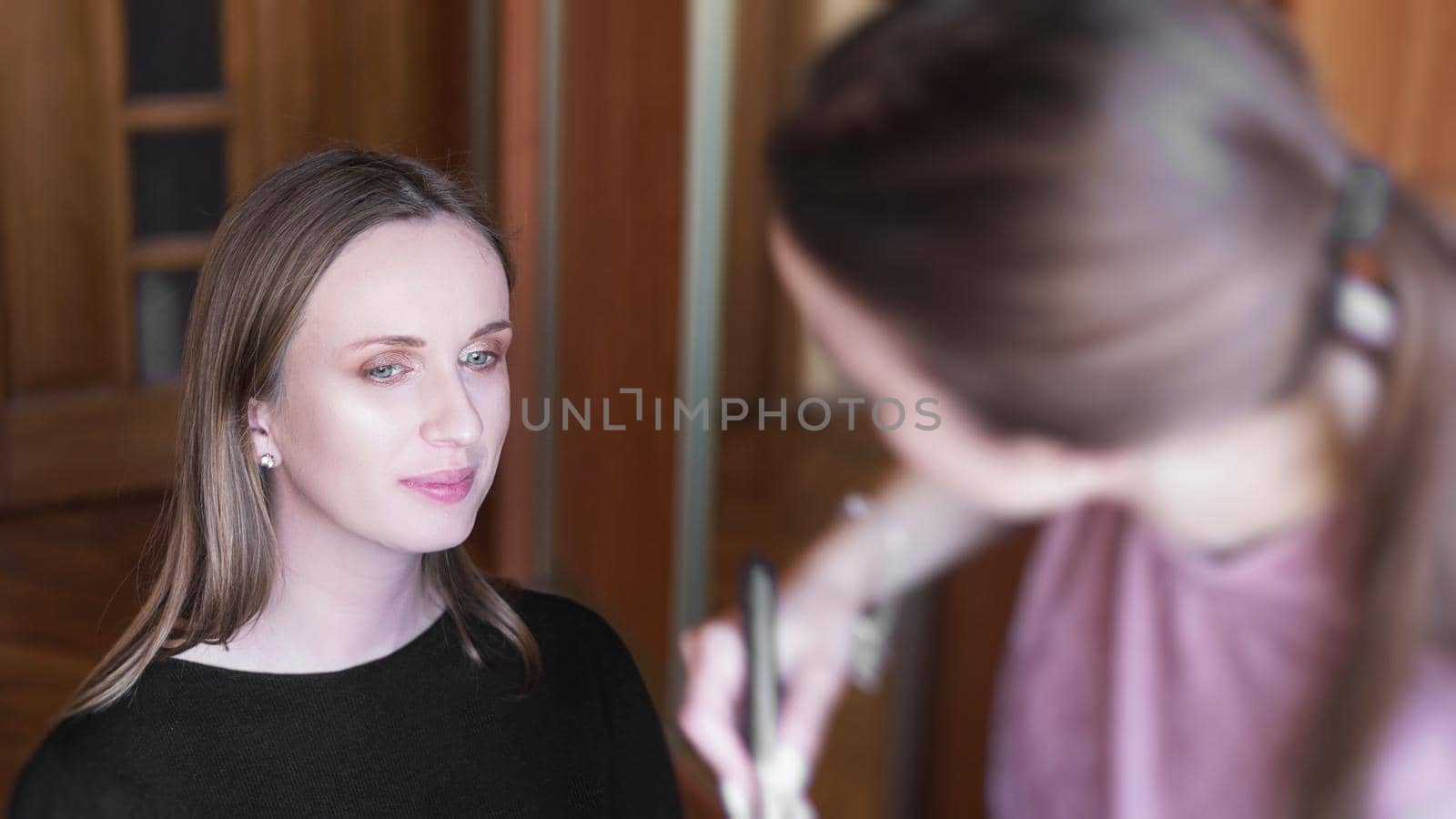 Process of making makeup. Make-up artist working with brush on model face. Portrait of young woman in home interior.