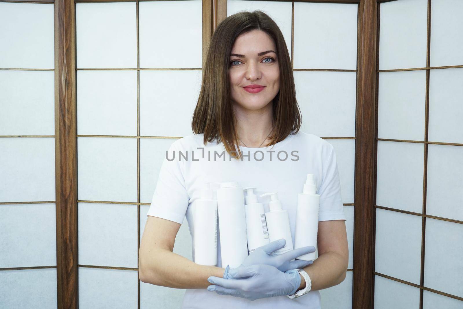 Master holds set of cosmetics - white bottles - Beautiful woman master in a beauty salon