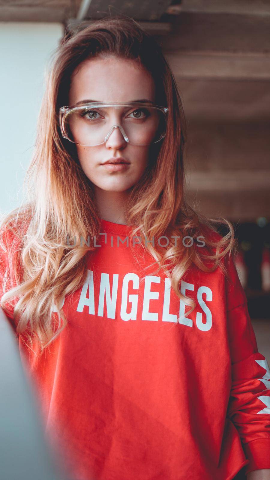 Fashion model wearing red hoodie with the inscription los angeles and big plastic glasses posing in the city at parking. Fashion urban outfit