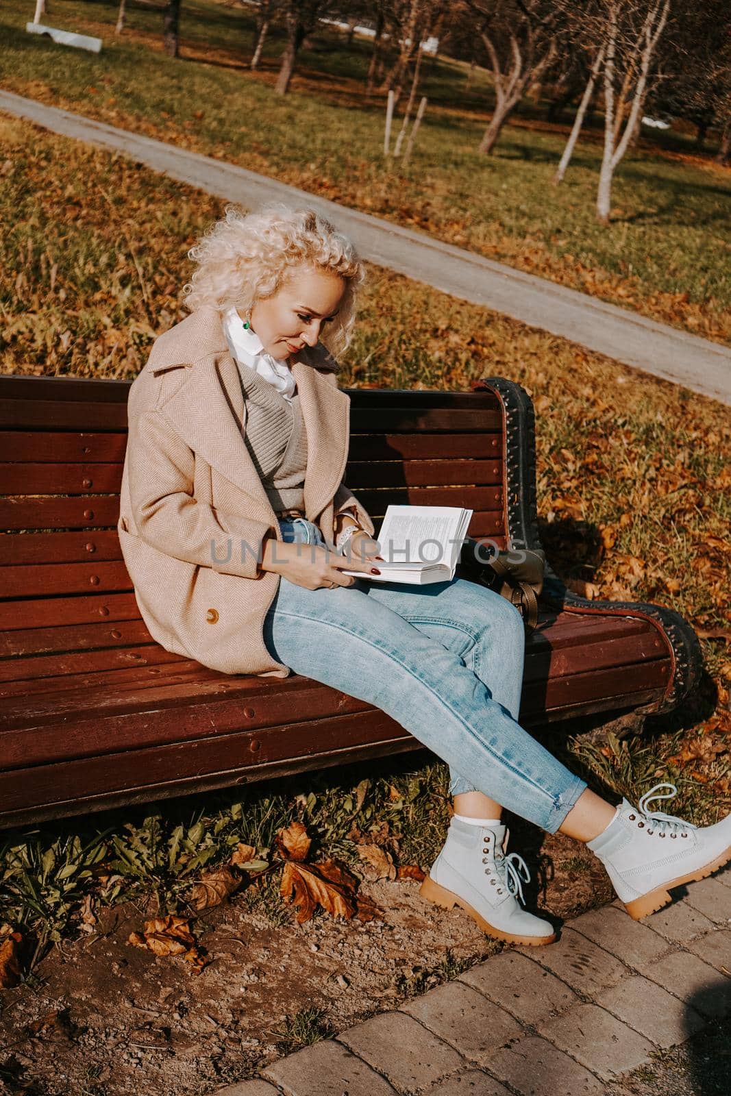 Woman reading a book on a park bench, leisure time in autumn park