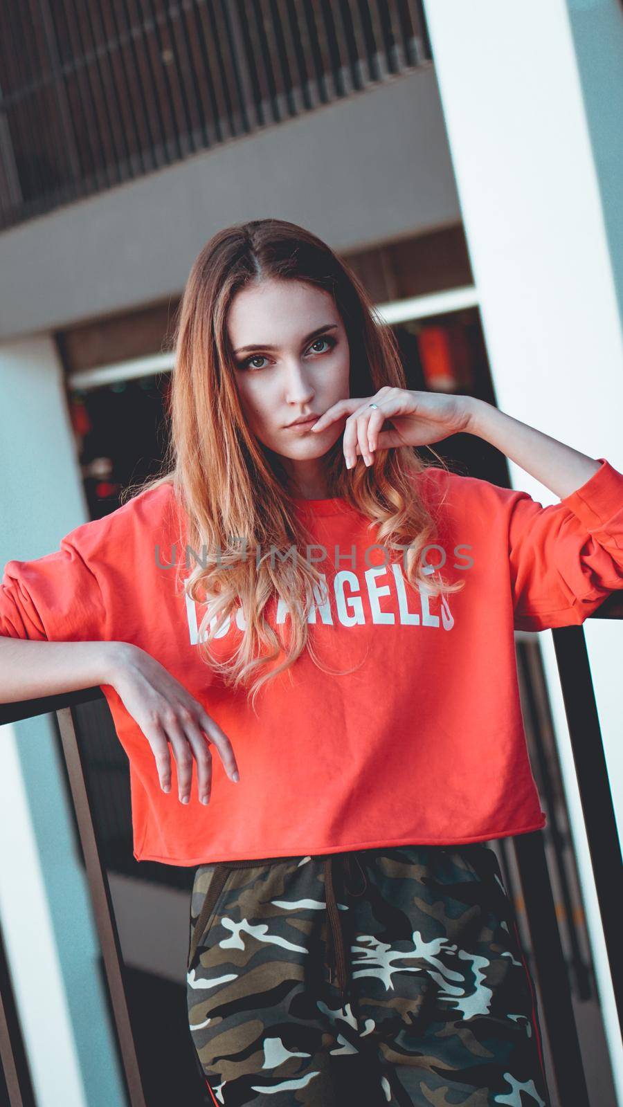 Fashion model wearing red hoodie with the inscription los angeles posing in the city at parking. Fashion urban outfit. Casual everyday clothing style