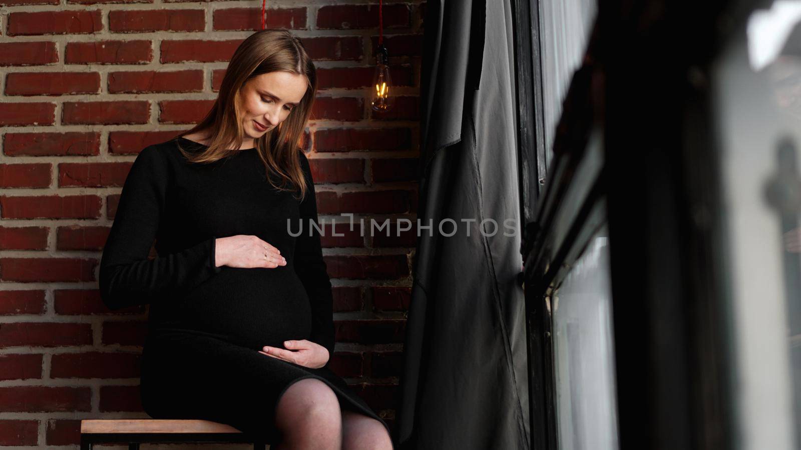 Young pretty pregnant woman in black dress in studio - loft interior