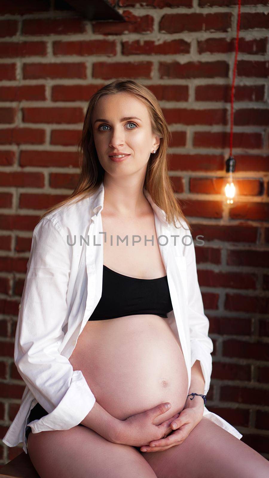 Beautiful young woman pregnant, in black lingerie and white shirt, brick wall by natali_brill