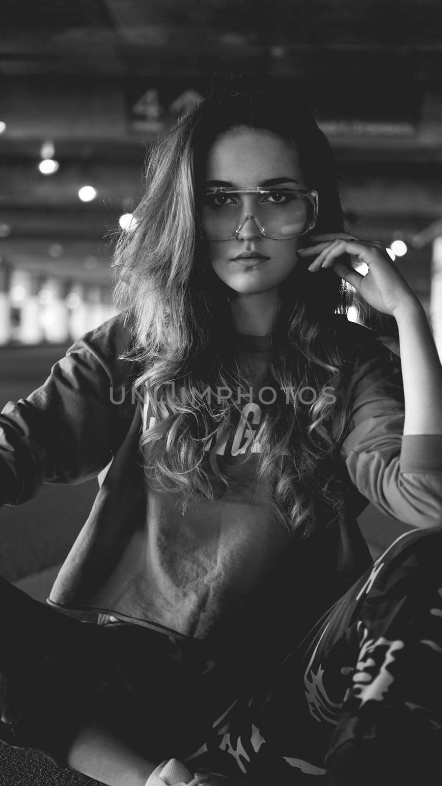 Pretty young woman in hoodie sitting on car parking. Wearing stylish urban outfit - Black and white photo