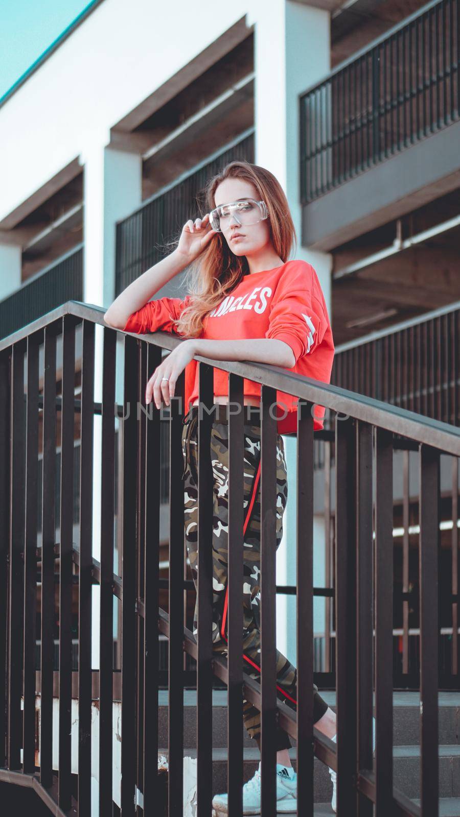 Fashion model wearing red hoodie with the inscription los angeles posing in the city at parking. Fashion urban outfit. Casual everyday clothing style