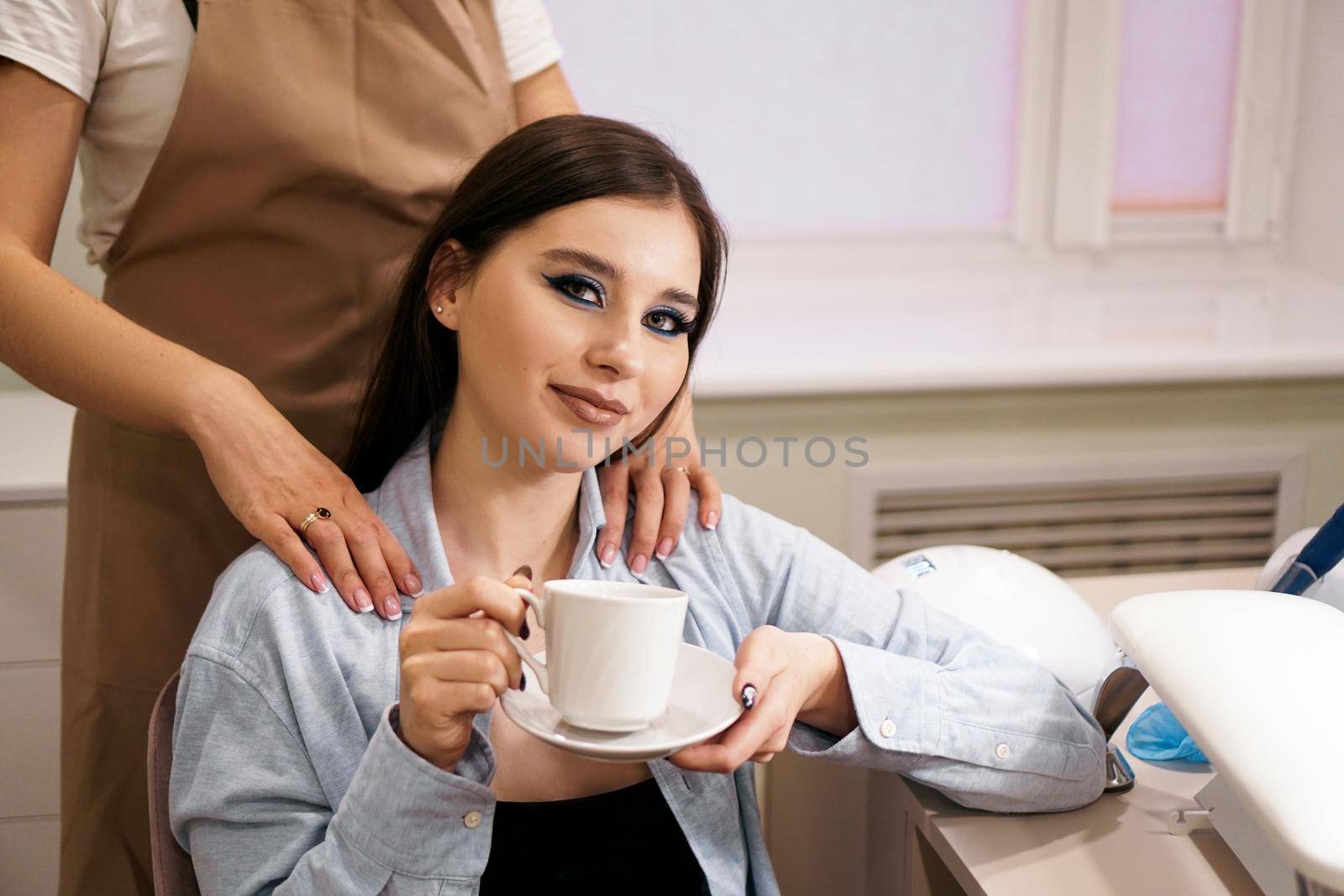 Beautiful woman getting manicure and massage at the same time in a beauty salon. She smiles and holds a cup of coffee. VIP client in a beauty salon