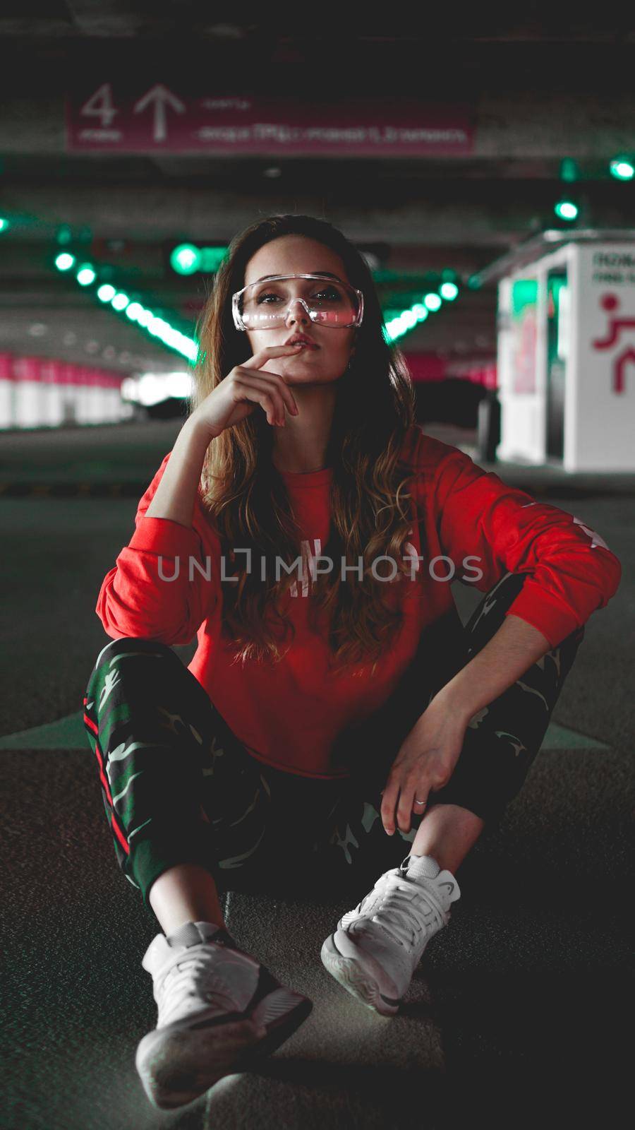 Pretty young woman sitting on car parking. Wearing stylish urban outfit by natali_brill