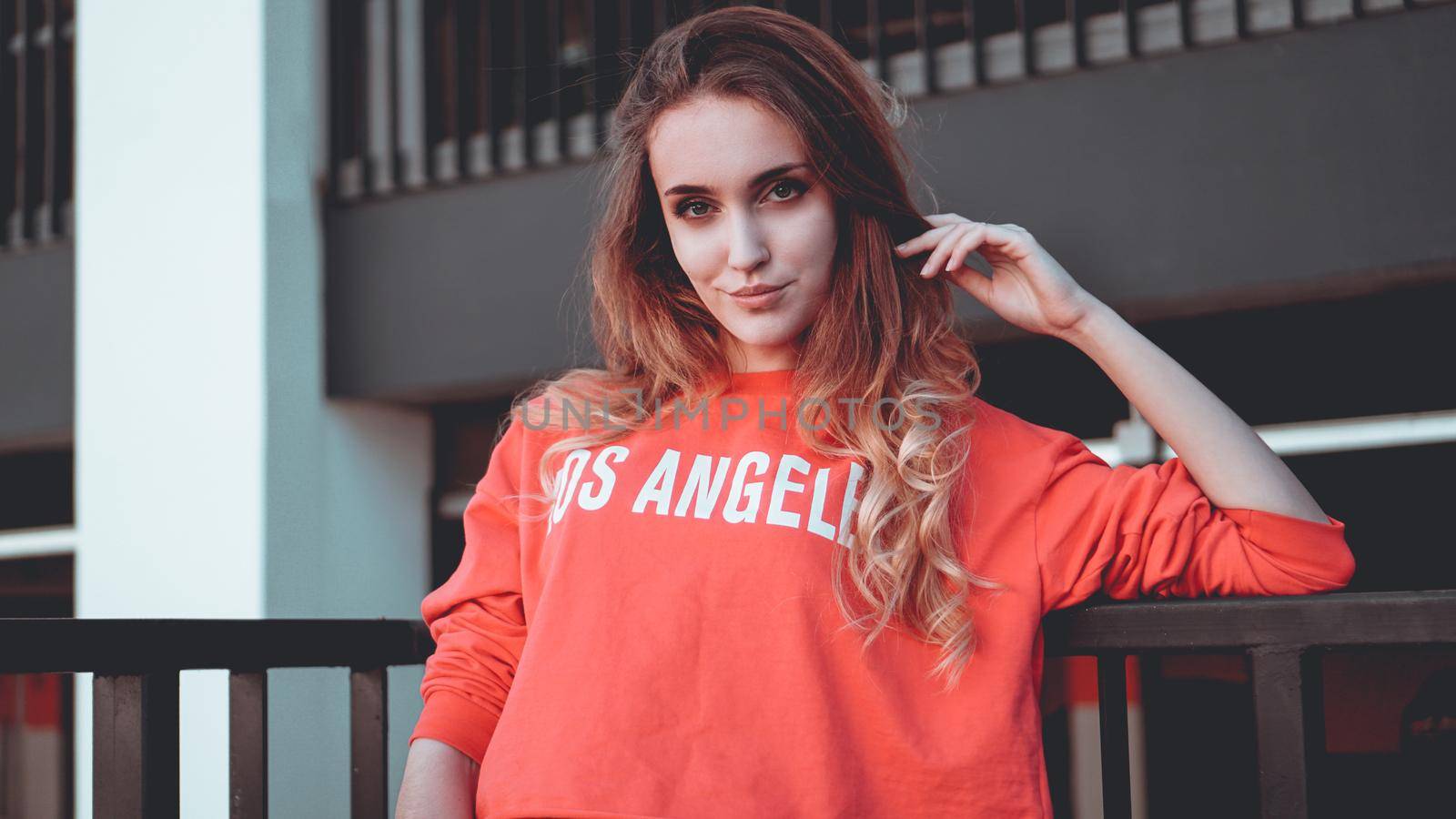 Fashion model wearing red hoodie with the inscription los angeles posing in the city at parking. Fashion urban outfit. Casual everyday clothing style