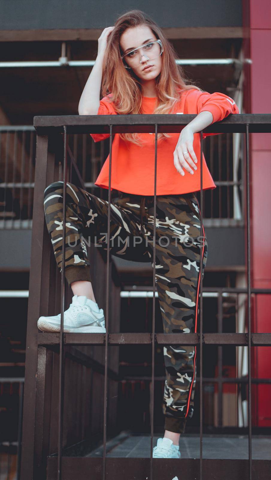 Fashion model wearing red hoodie with the inscription los angeles posing in the city at parking. Fashion urban outfit. Casual everyday clothing style