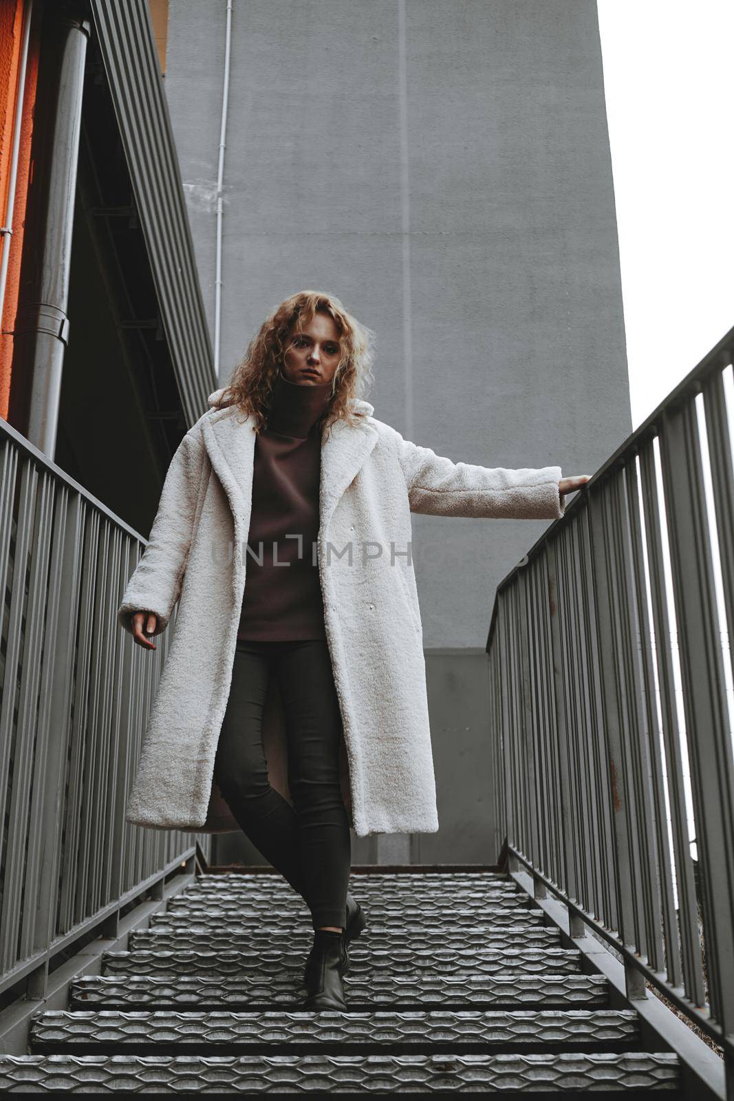 A girl with red curly hair in a white coat poses on the parking stairs by natali_brill