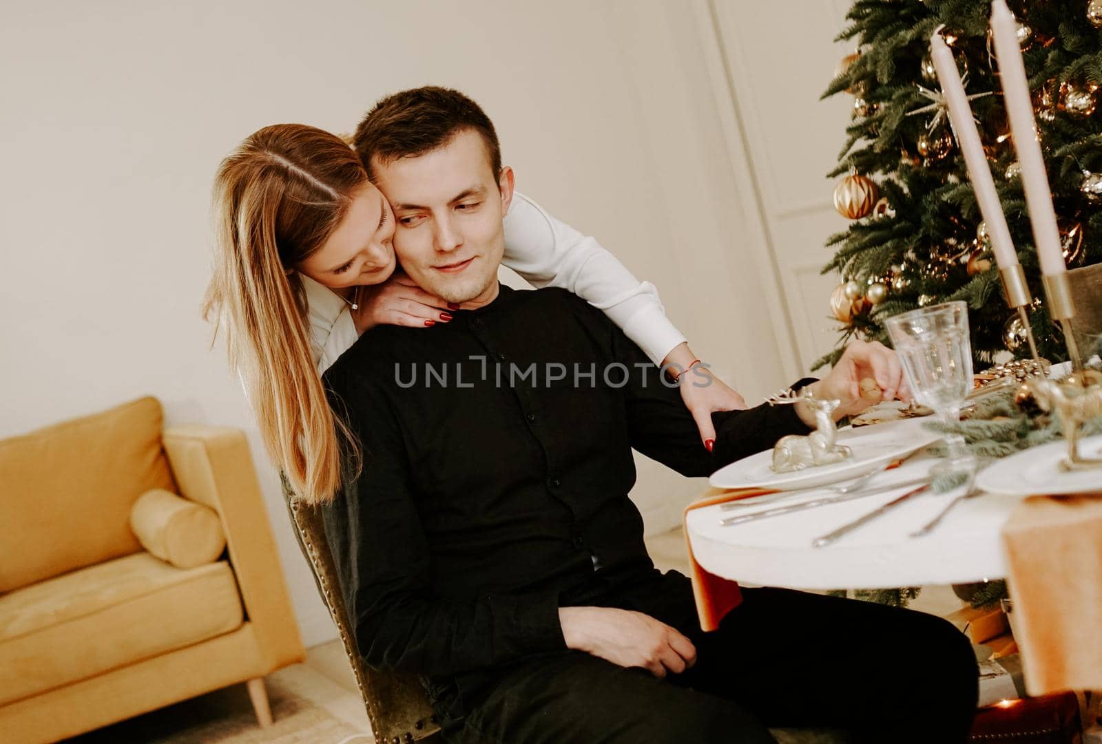 Young happy couple in love hugging.Young man and woman celebrate Christmas holidays together in a bright room with table decorated for xmas