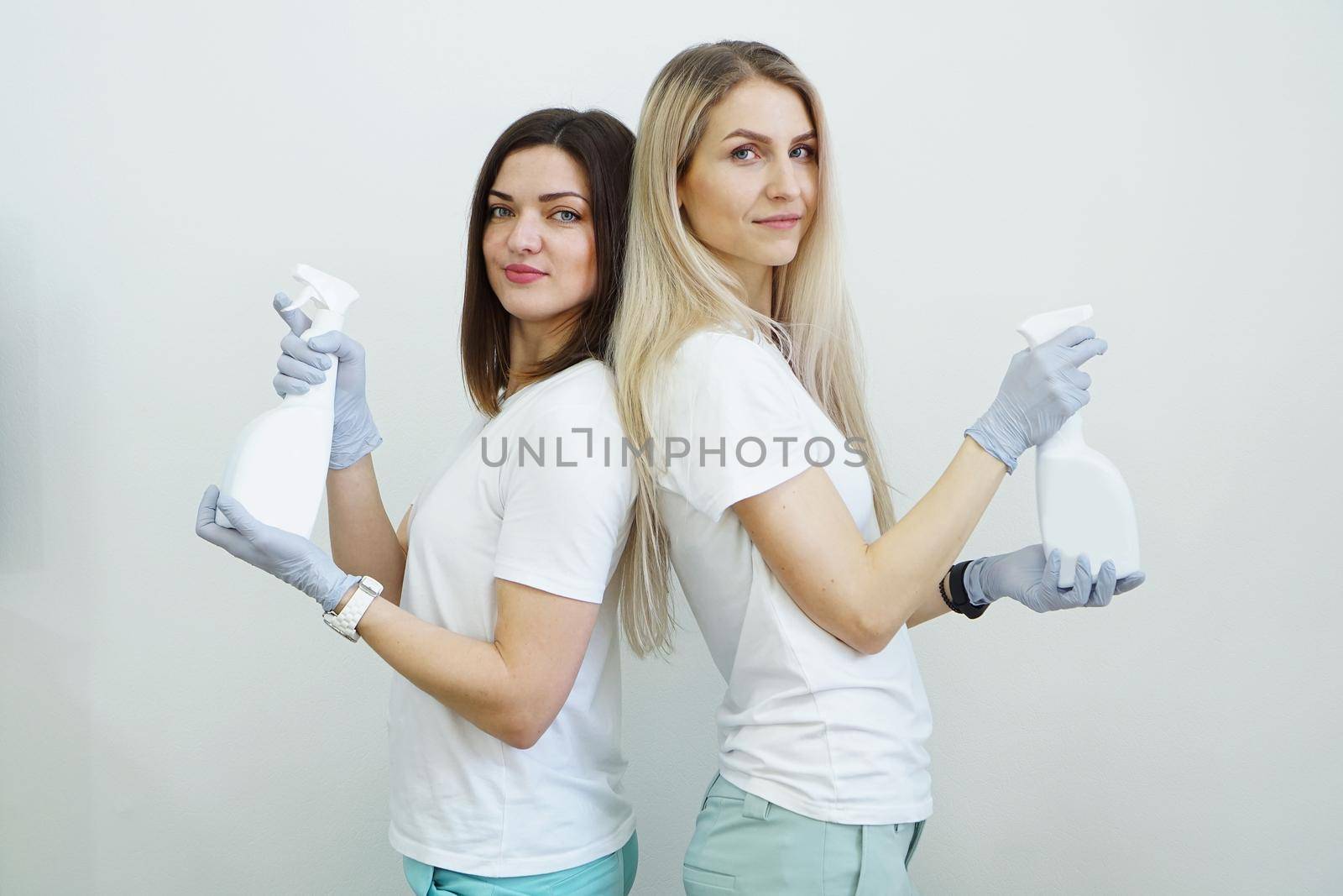 Two women hold spray bottle with antiseptic or detergent like guns. Health or cleaning concept Covid-2019