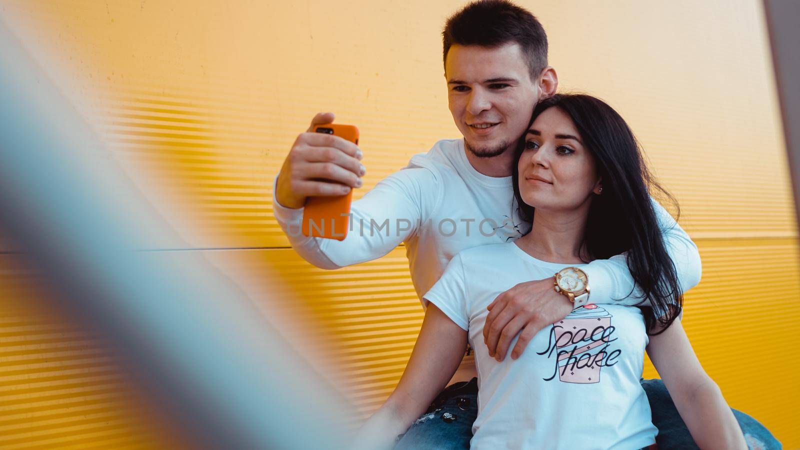Young lovely couple posing together while making selfie on smartphone over yellow background
