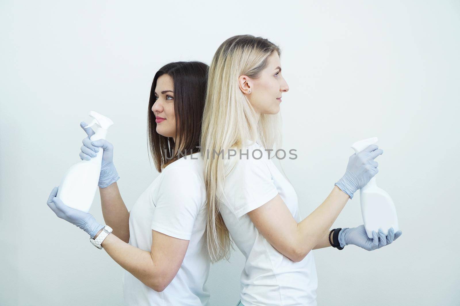 Two women hold spray bottle with antiseptic or detergent like guns. Health or cleaning concept Covid-2019, on white background