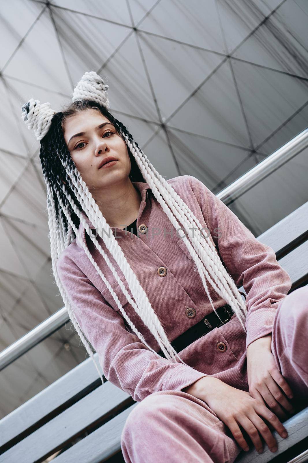 Young woman with futuristic looks. Girl with black and white dreadlocks or pigtails. Against the background of a futuristic building
