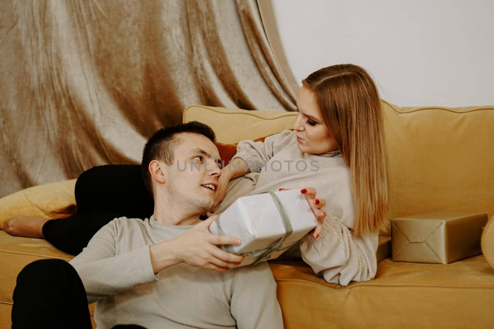 Beautiful young couple holding a gift box while sitting on couch at home - soft preset