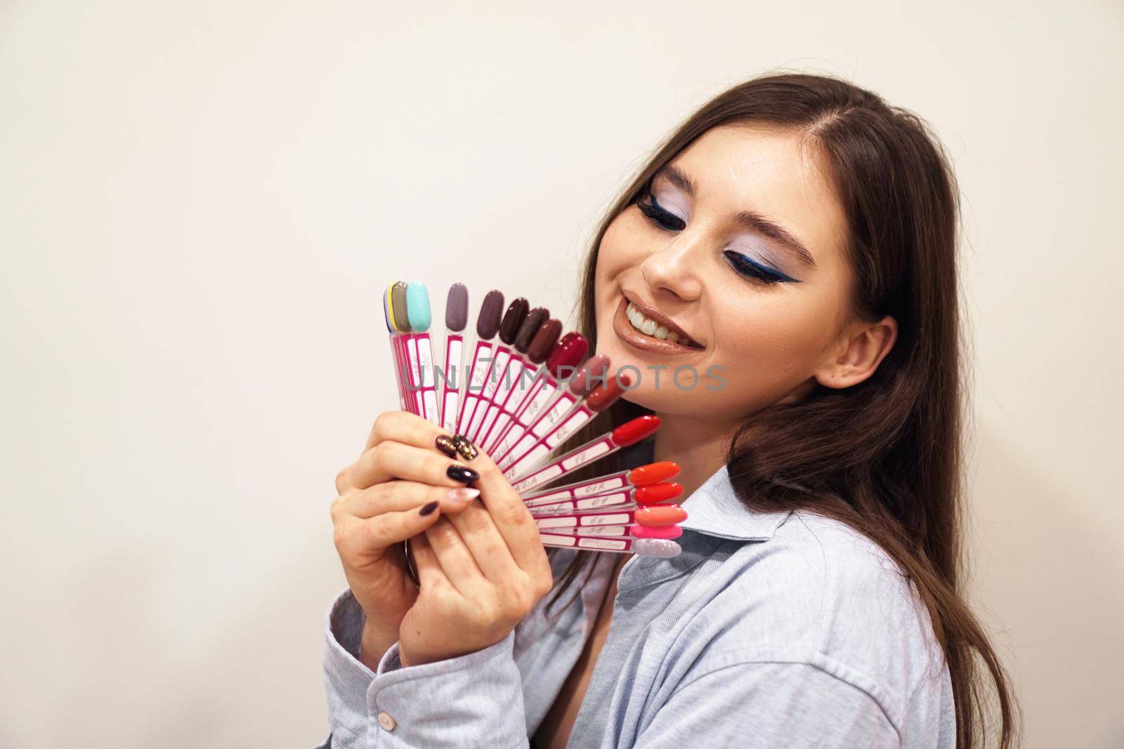 Pretty young woman smiling, holding a manicure and pedicure nail polish palette in a hand. Cosmetic products. Beauty salon.