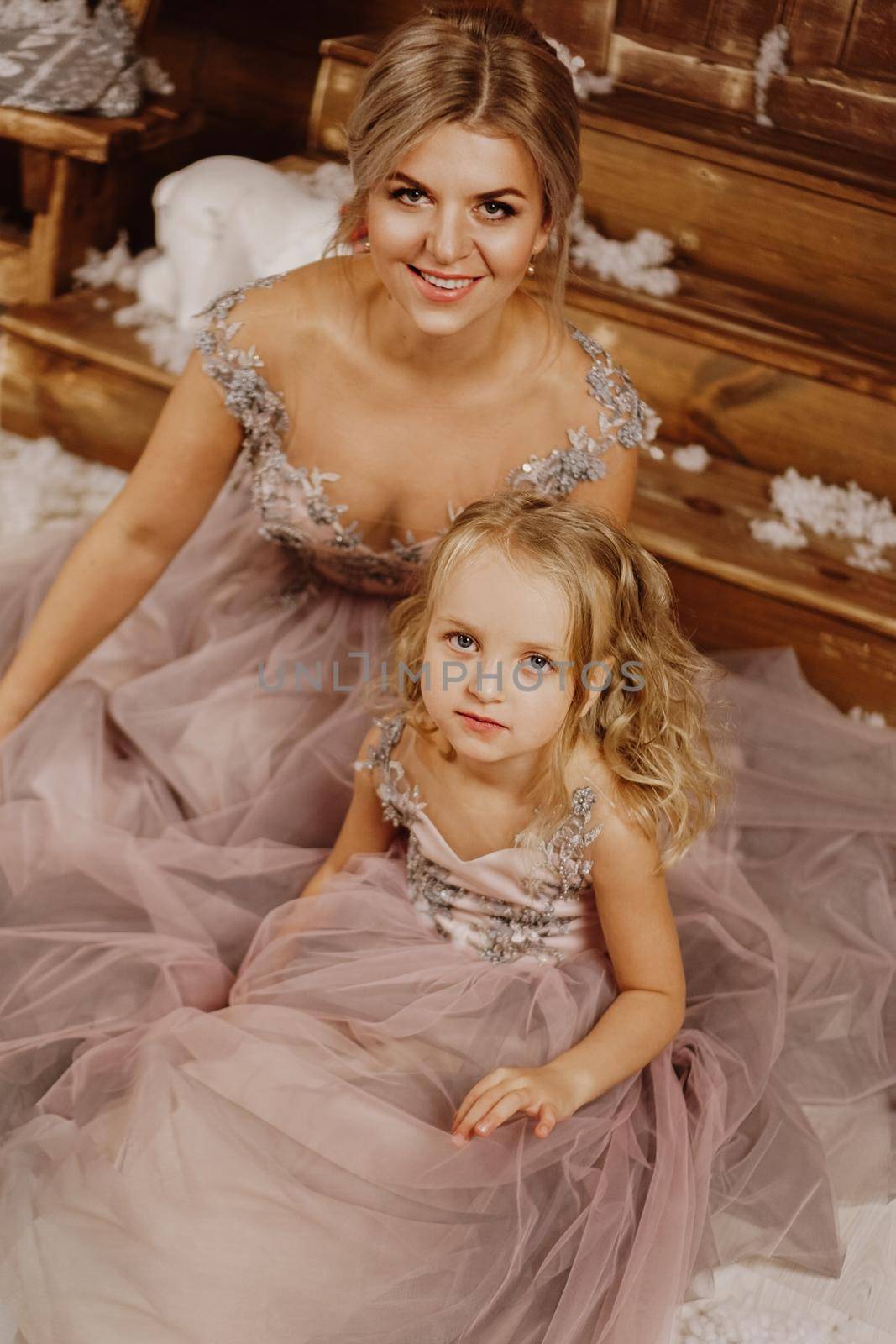 Mother and her daughter in pink dresses lying on the carpet near the Christmas decorations. Overhead