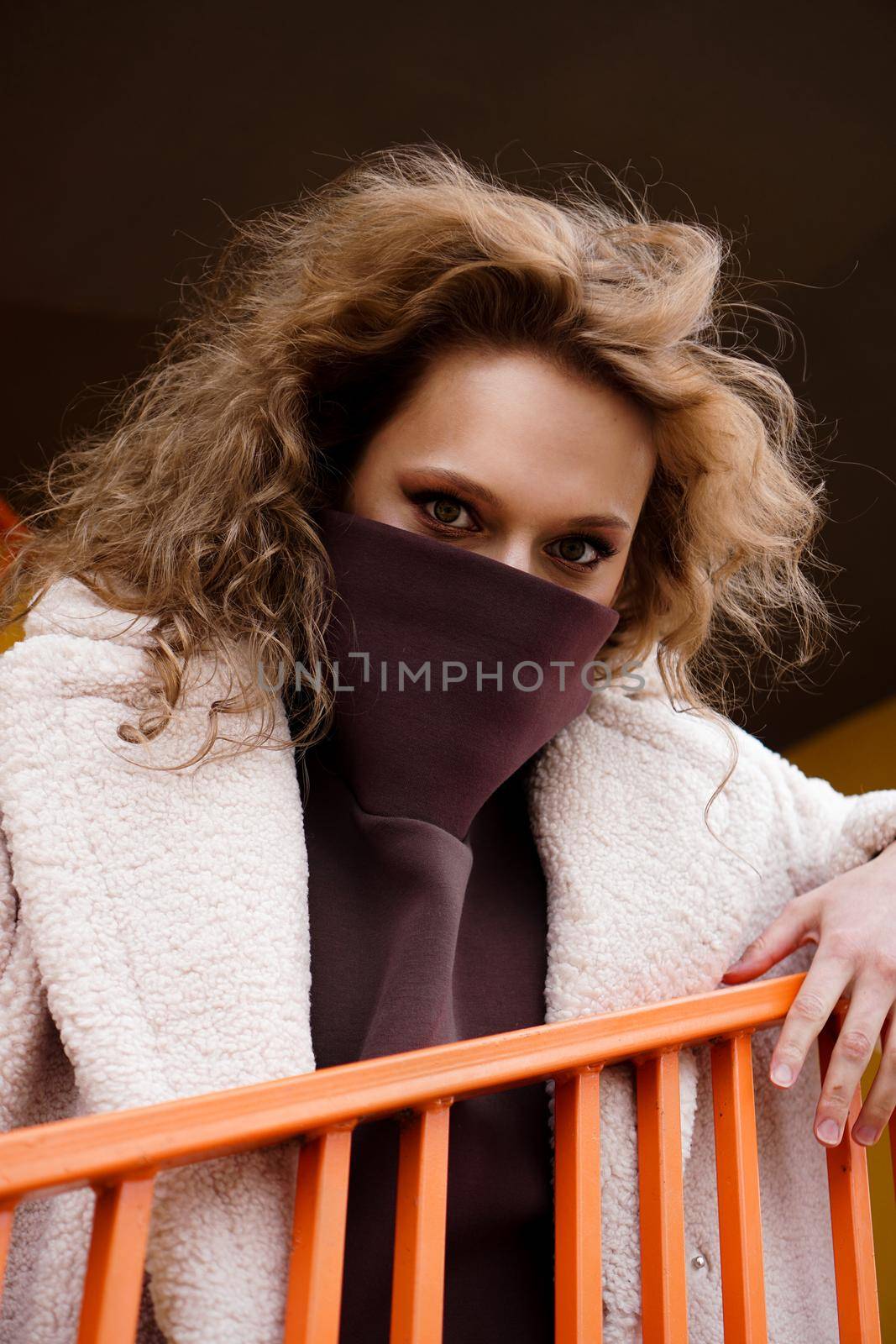 A girl with red curly hair in a white coat poses on the yellow parking stairs by natali_brill