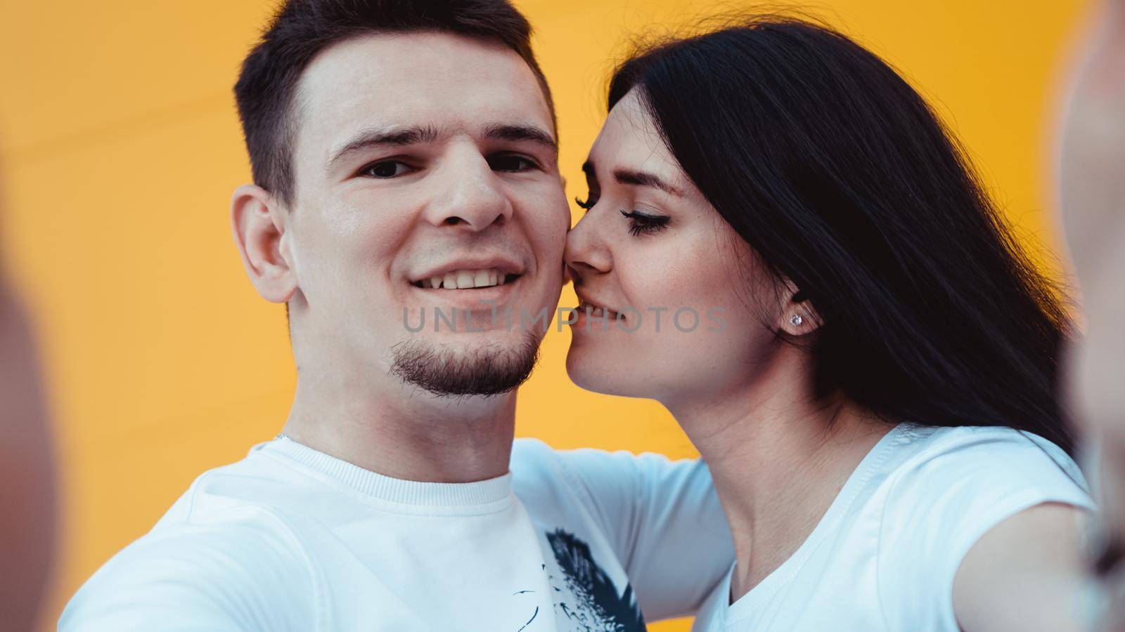 Young lovely couple posing together while making selfie on smartphone over yellow background