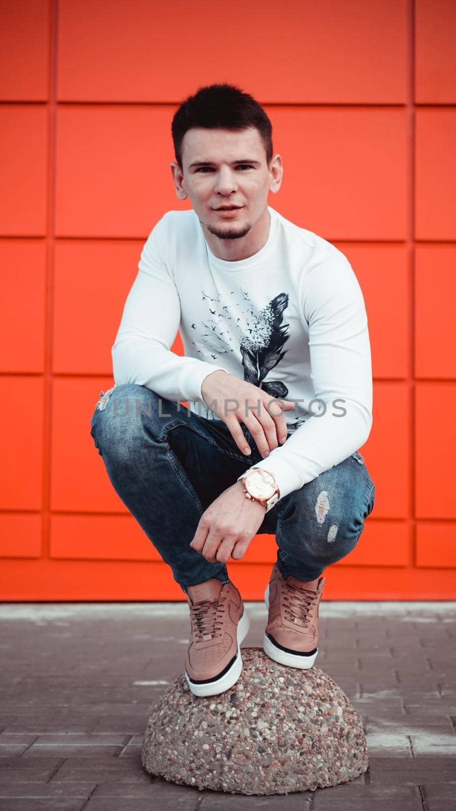 Handsome young man in a white sweater and blue jeans on red background