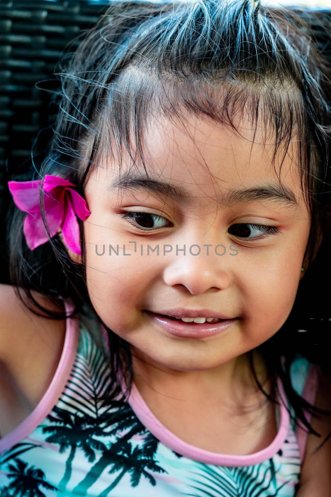 Little girl with large pink flower behind ear. Pretty asian child portrait with flower behind ear smiling by billroque