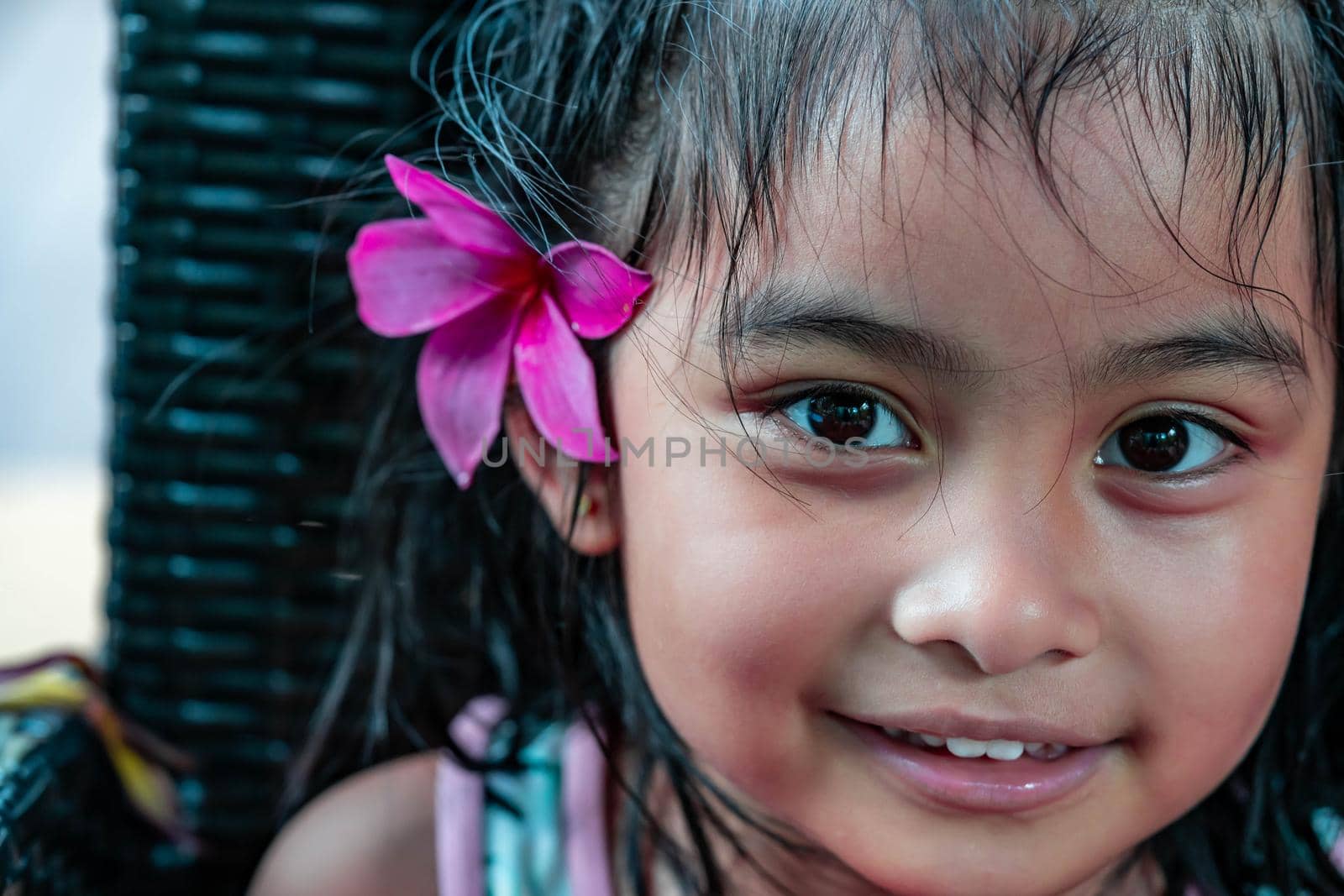 Little girl with large pink flower behind ear. Pretty asian child portrait with flower behind ear