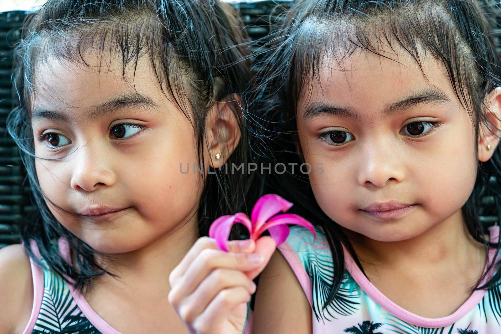 Pretty child twins holding a pink flower. Pretty asian twins portrait with flower and smiling