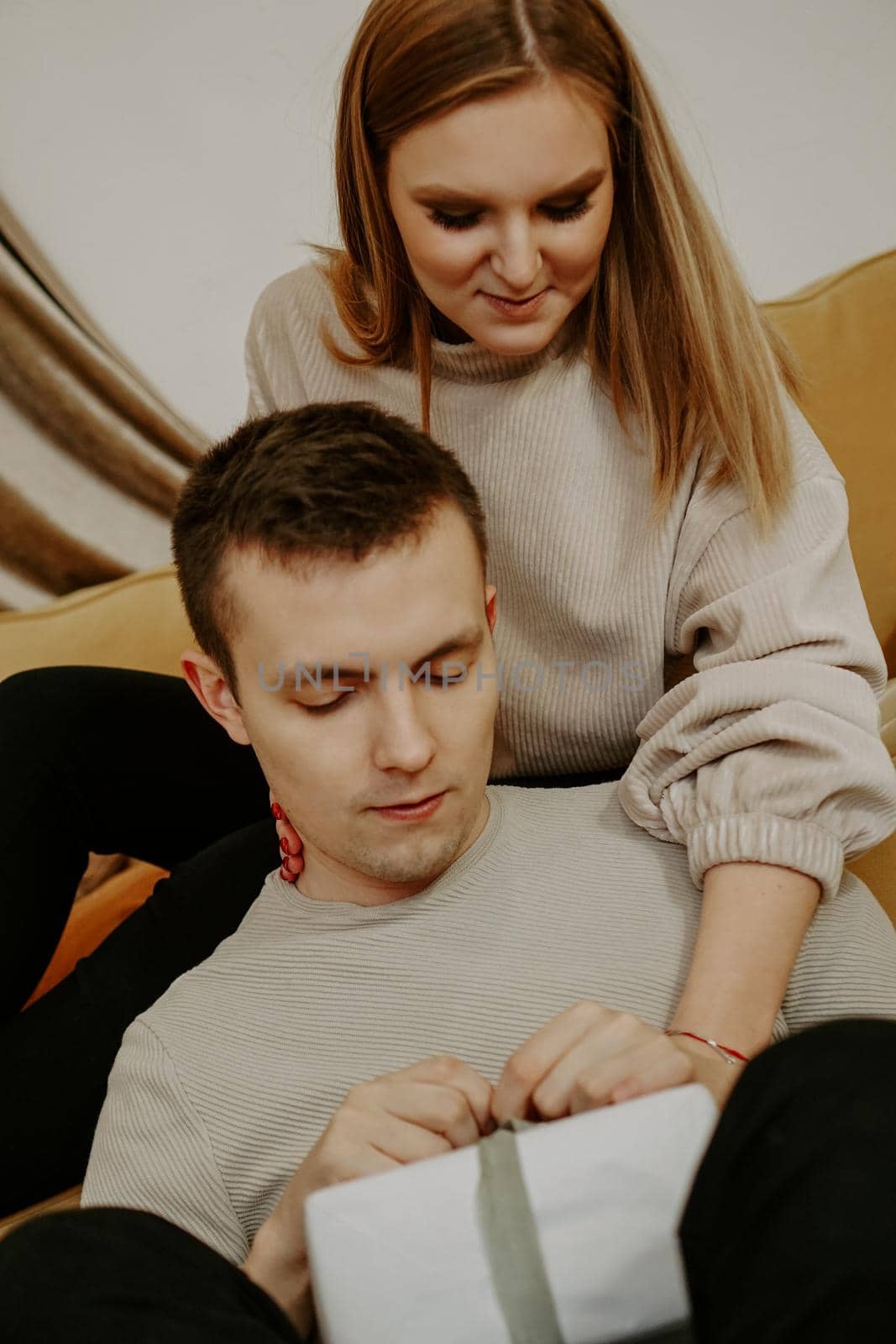 Beautiful young couple holding a gift box while sitting on couch at home - soft preset