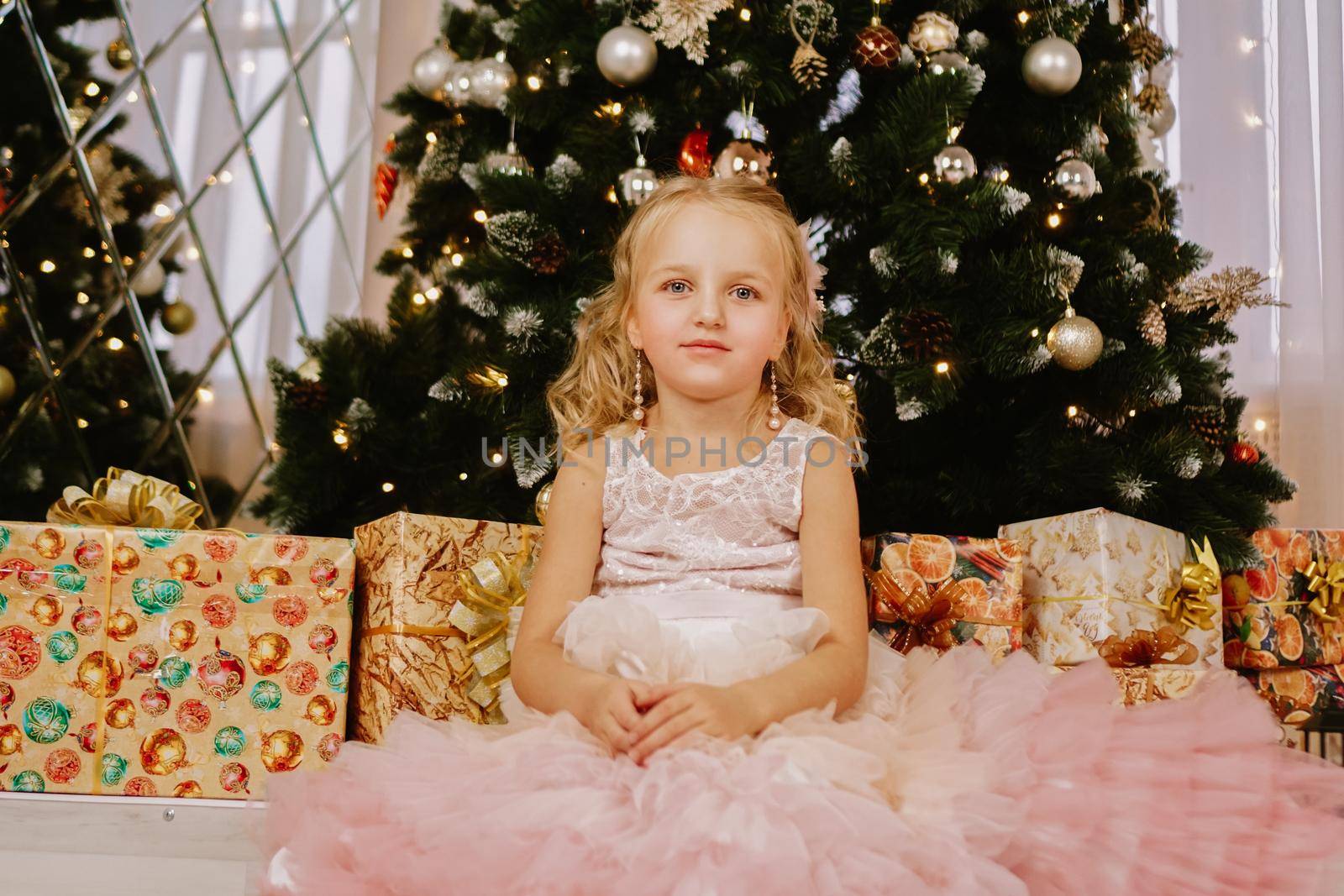 Girl in a pink dress near the Christmas tree and boxes with gifts