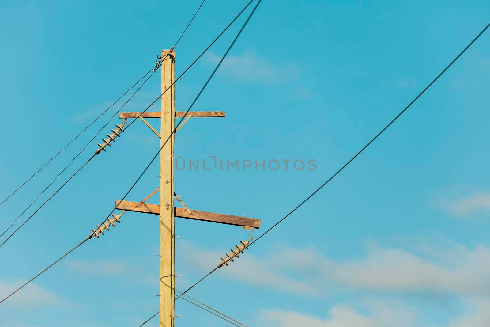 Photograph of a wooden telephone post and cables against a blue sky