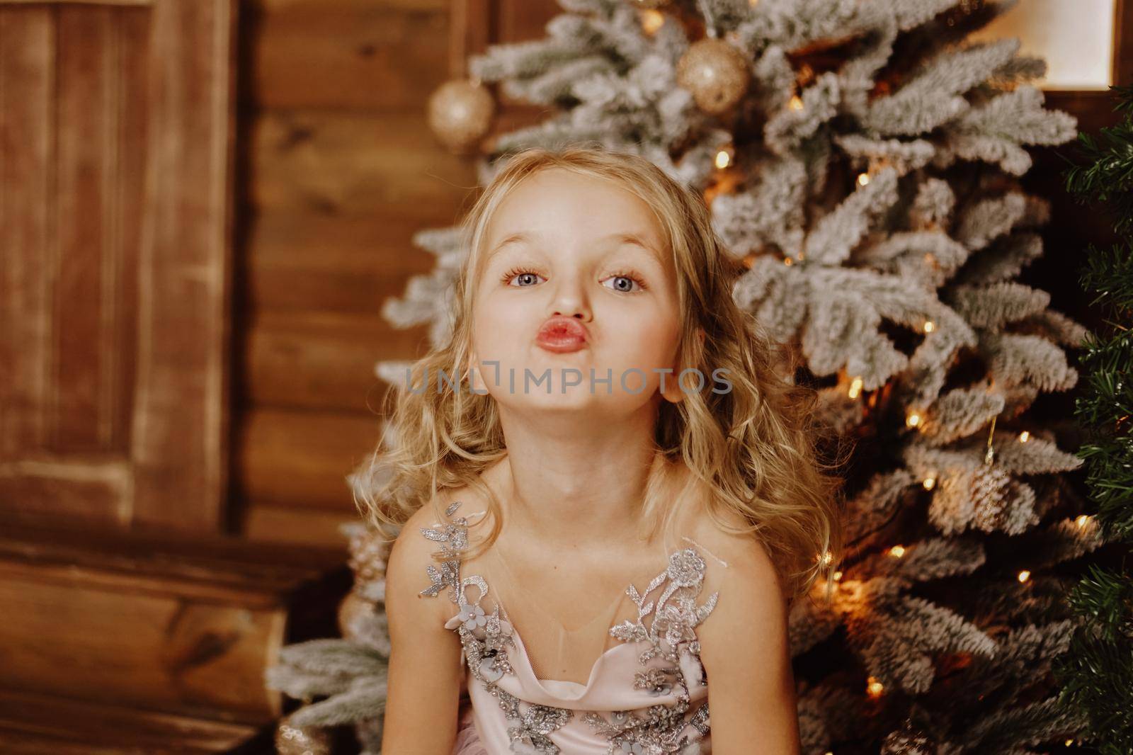 Happy Little girl in a pink dress grimaces on the background of the Christmas tree