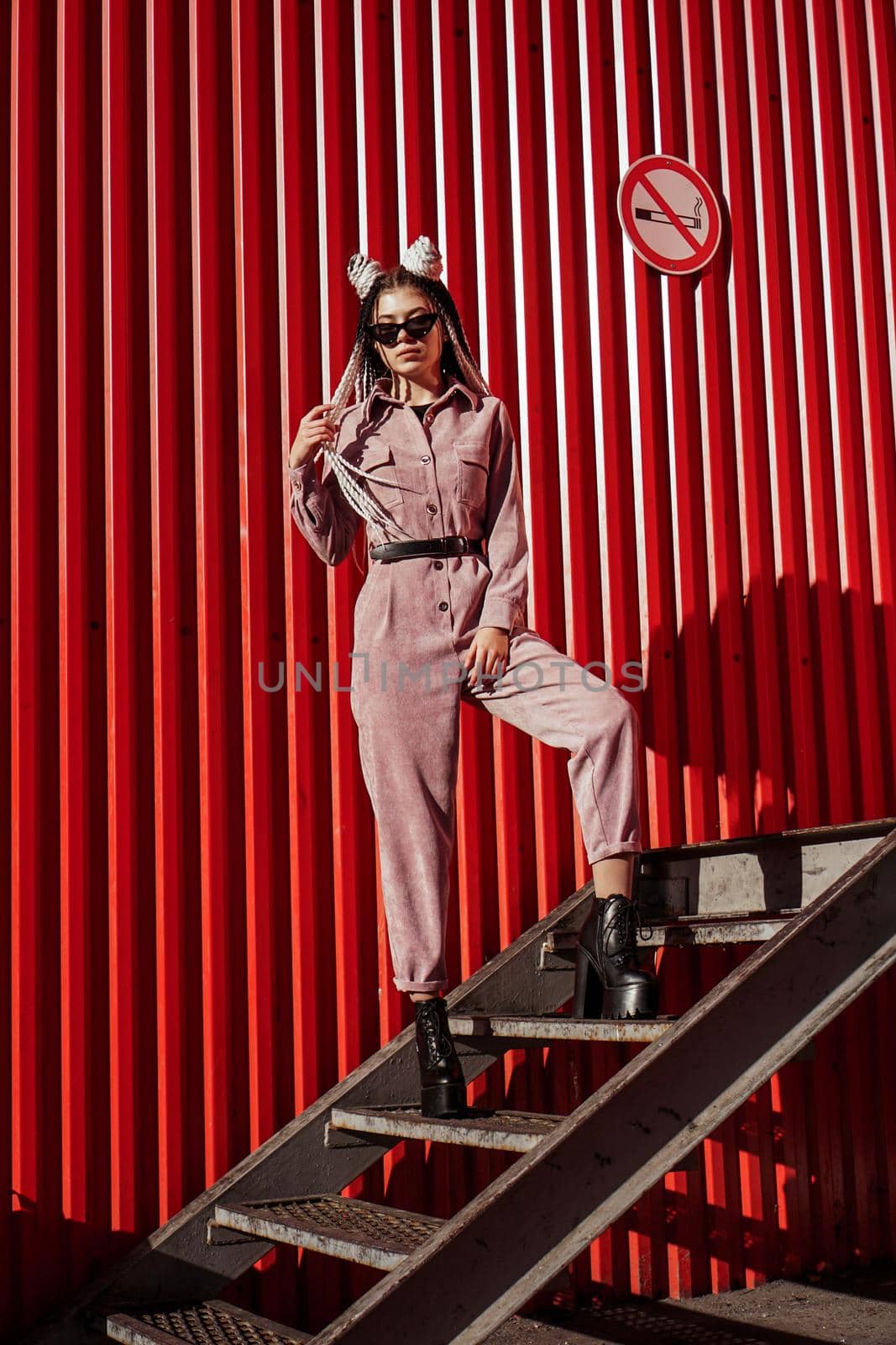 Beautiful girl over urban wall. Sunny day. Girl in sunglasses and pink jumpsuit