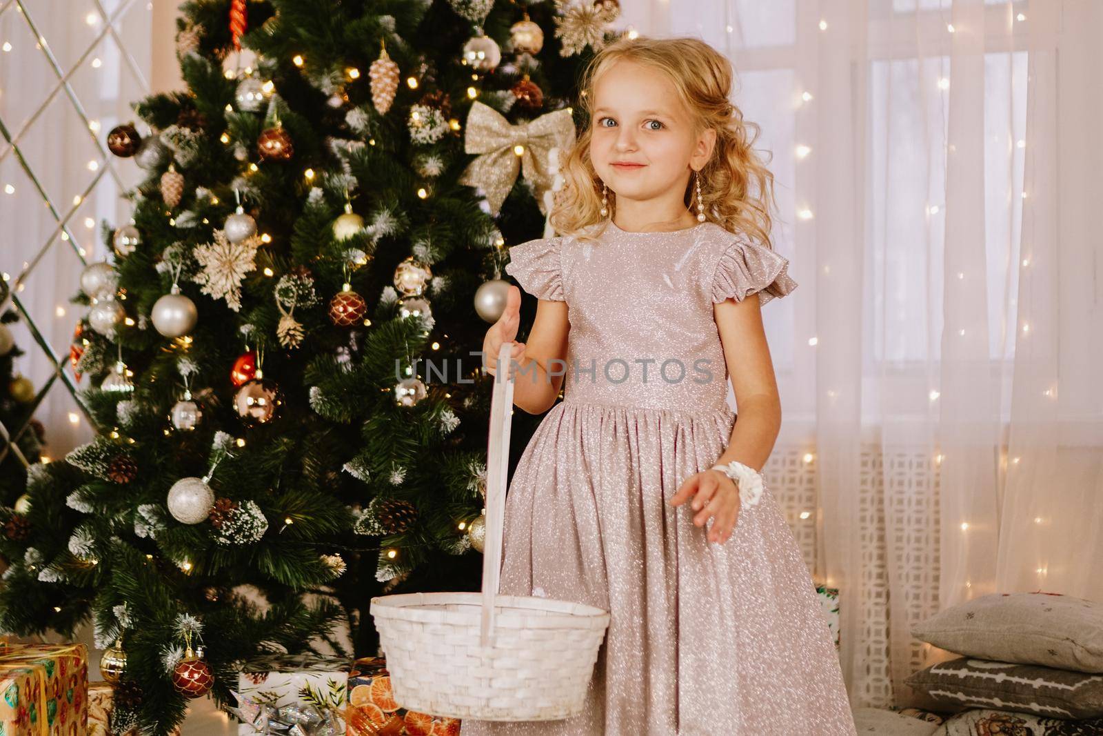 Girl in a pink dress with a wicker basket near the christmas tree