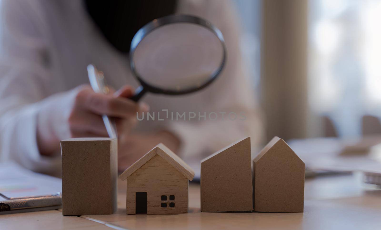 Woman bank officer or appraiser using magnifying glass to check miniatures house model. The concept of searching for living and checking quality inspection of housing or assets.